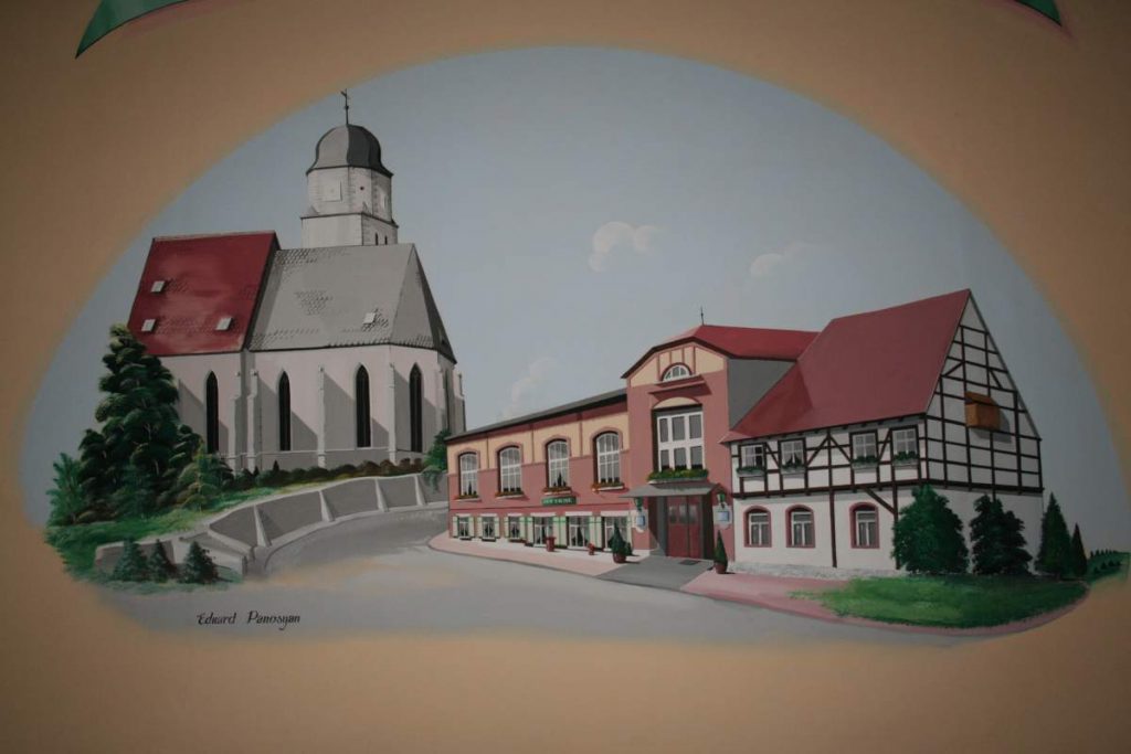 Nástěnná malba od gruzínského malíře Eduarda Paniosana. Zobrazuje kostel a historický hostinec ve městě.